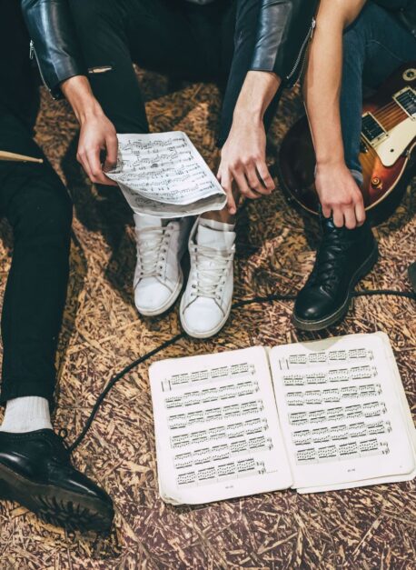 Repetition of rock music band. Cropped image of guitar players and drummer are sitting on the floor at rehearsal base with notes. Top view